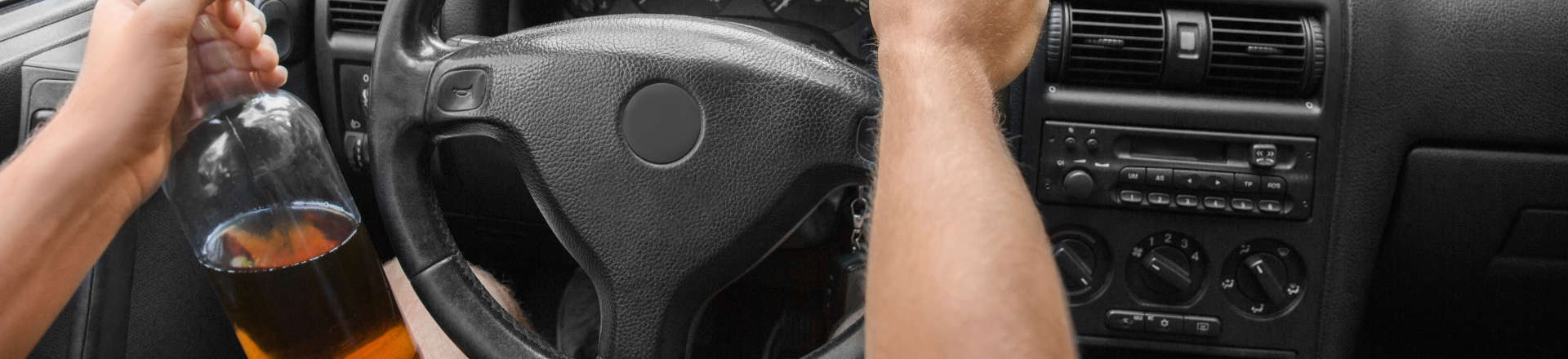 a driving person with a bottle of alcohol in their hand