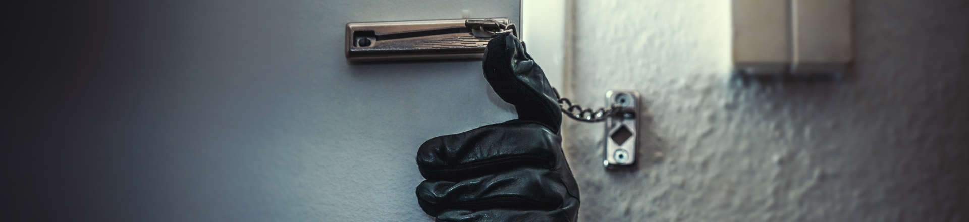 hand in a black glove trying to open a security door chain from outside
