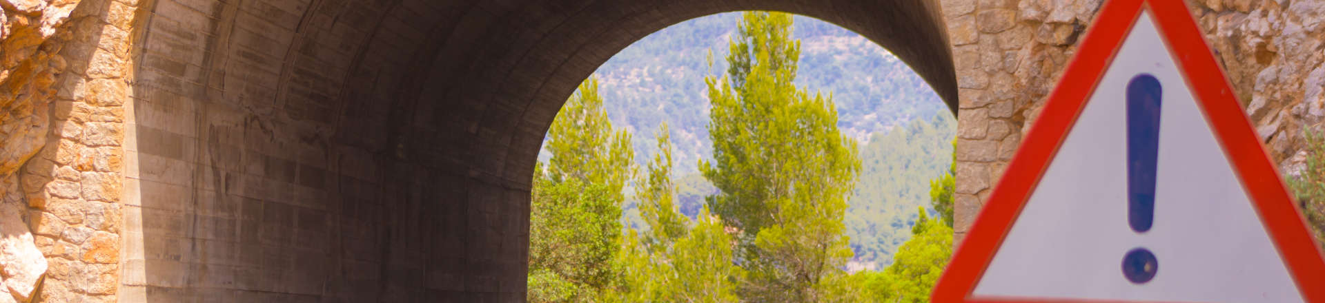 A triangular road sign with exclamation mark in front of underpass