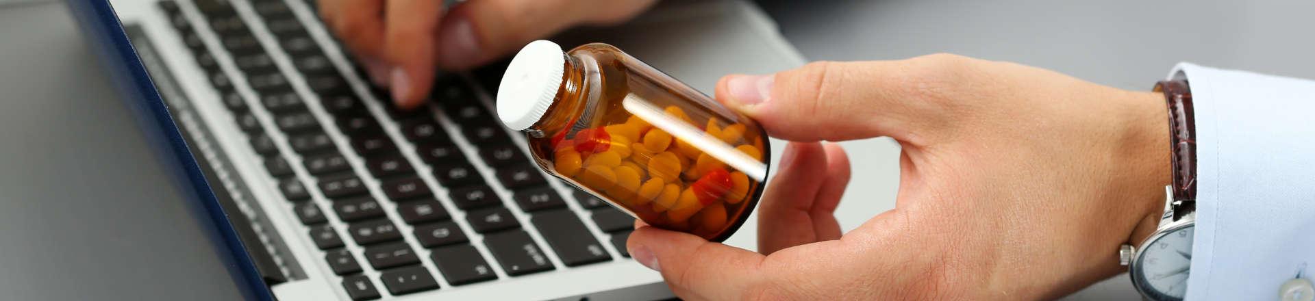 a person at a laptop holding a bottle with medicines in their hand