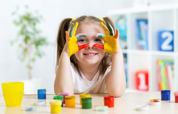 A little girl with hands painted with different colors while playing a a day care center