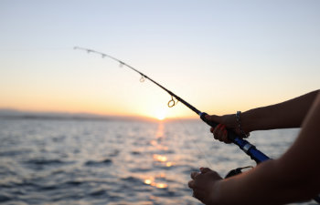 woman enjoys fishing on boat sailing in sea with light waves at sunset