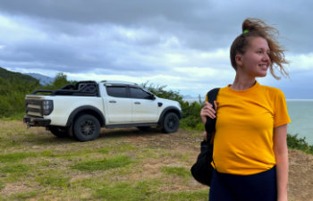 a woman in a yellow blouse stands against a white car