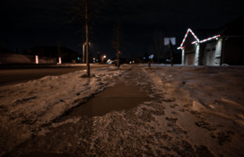 ice and snow on a sidewalk at night with streetlight reflecting off the slick surface