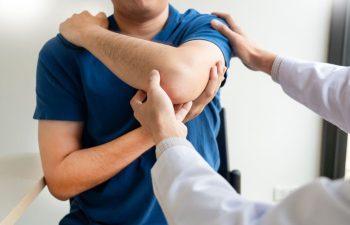 A doctor examines a patient's elbow while the patient holds his arm across his chest.