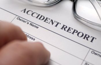 A close-up of a hand filling out an accident report form, with eyeglasses placed nearby on the document.