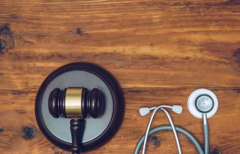 A judge's gavel and a stethoscope are placed side by side on a wooden surface.