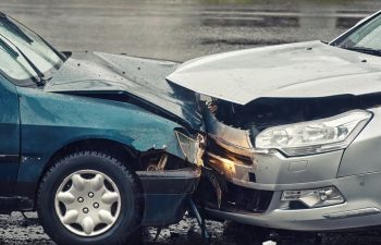 Car accident on wet road during rain, head on collision side view. Two cars damaged after head-on collision, car crash. Car crash on the street, damaged cars after collision. Traffic rules violation